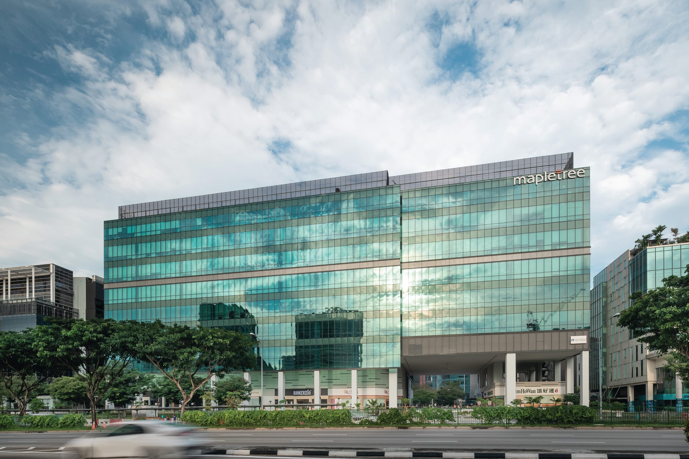A modern glass office building with the "mapletree" logo against a cloudy sky.